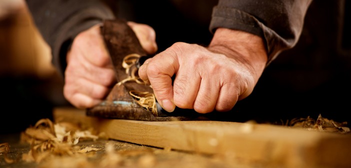 Senior man or carpenter doing woodworking planing the surface of a plank of wood in his workshop with a manual plane as he enjoys his creative hobby